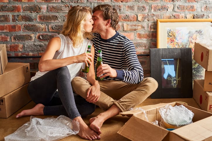 Romantic couple holding beer bottles while kissing at new home.