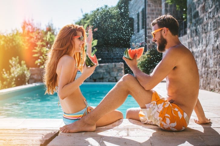 Attractive young couple relaxing on poolside. Eating watermalon. Wearing swimsuits.