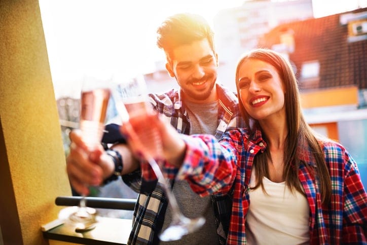 Young casual hipster couple celebrating with champagne on apartment balcony