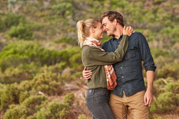 Romantic young couple embracing on field. Loving male and female partners spending quality time. They are wearing casuals.