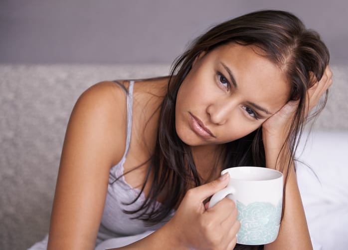brunette woman just waking up and drinking coffee in bed