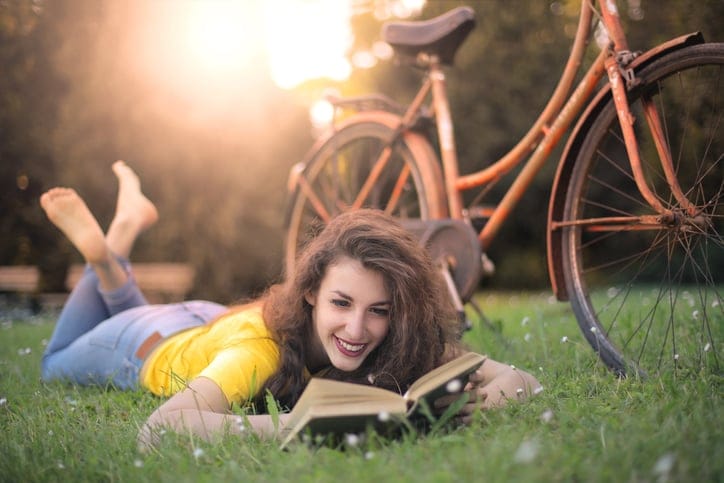 Woman laying in the grass reading a book.