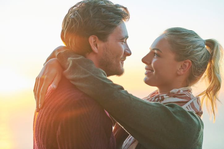 Side view of romantic young couple embracing against sky. Loving male and female partners are spending quality time together. They are wearing casuals during sunset.