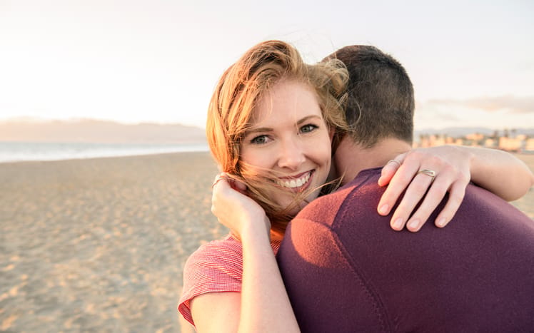 The young couple on the beach and the woman has her hand on the man's shoulder