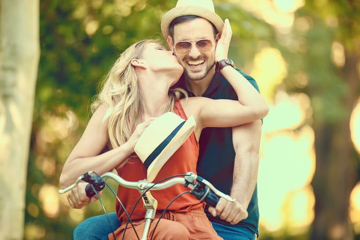 Portrait of happy young couple riding a bike in the park.