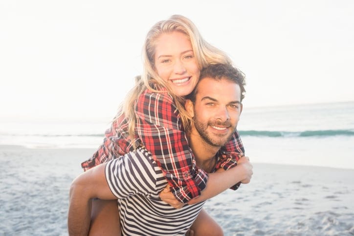 Portrait of a young man piggybacking beautiful woman on the beach