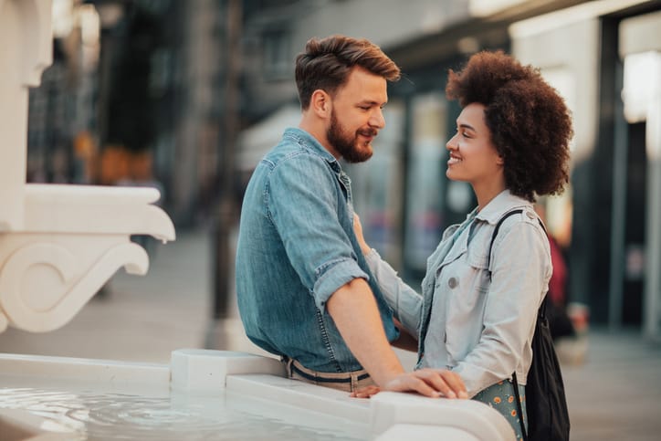 Man sitting on the edge of the fountain is looking at beautiful african girl