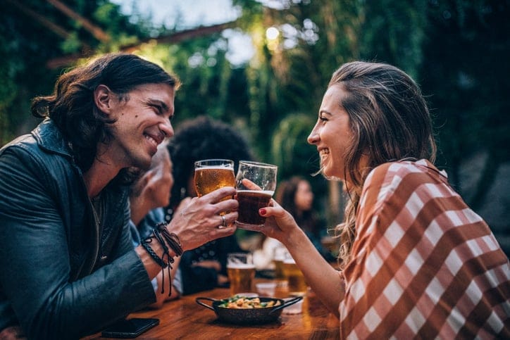 Happy couple cheersing beer at a garden pub.