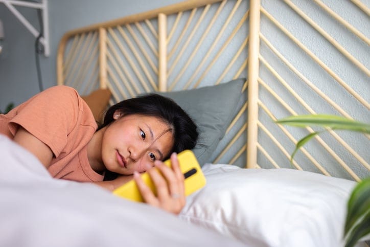Woman laying in bed on her phone.