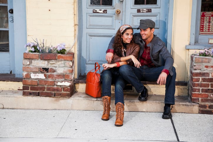 Young affectionate couple sitting on doorstep outside small town shop.