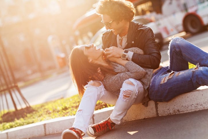 Close up of a happy young couple sitting on the sidewalk