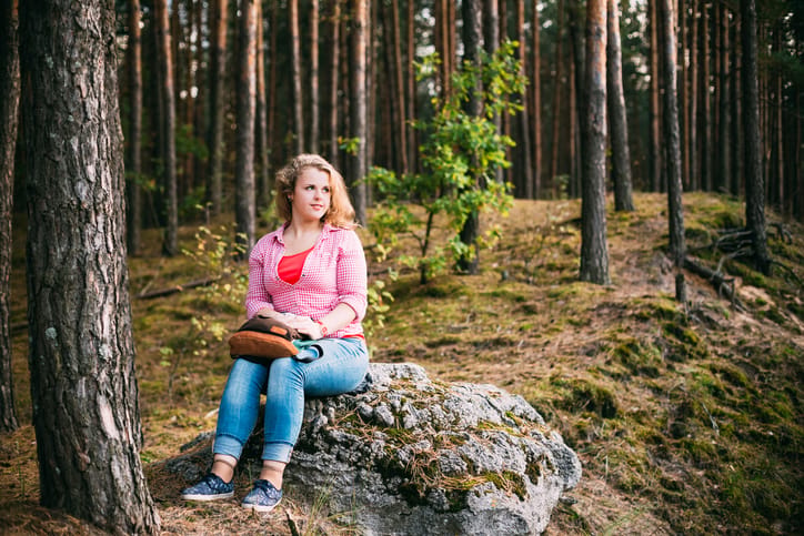 Beautiful Plus Size Young Woman In Shirt Sitting on Stone inSummer Forest