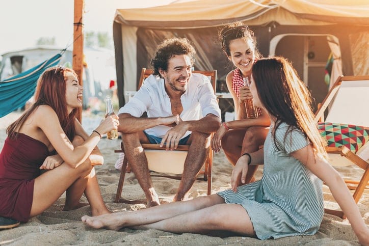 Group of young people chatting and drinking beer outdoors on a summer camp.