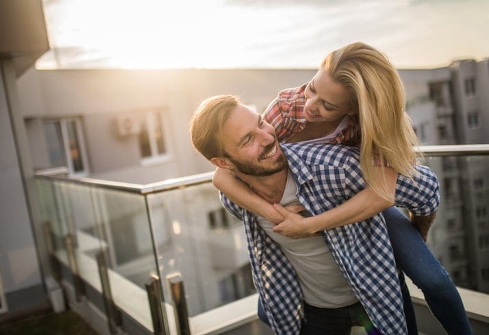 Young happy couple having fun while piggybacking on a terrace at sunset.