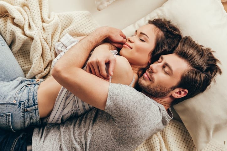 High angle view of beautiful happy young couple hugging while sleeping on bed