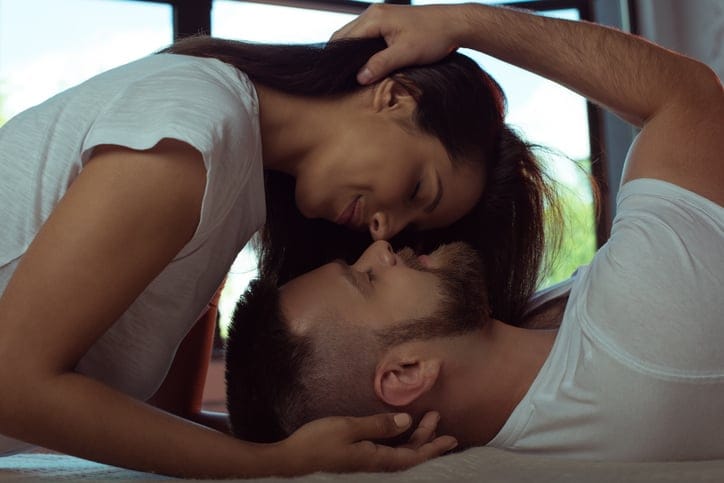 tender young couple with closed eyes hugging and kissing in bed