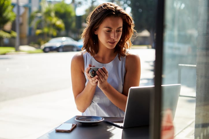Young white woman with coffee looks at laptop outside a cafe