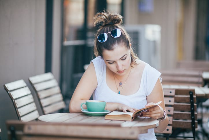 Girl Drinking Coffee and Reading Book in Cafe