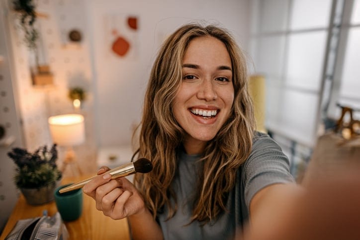 Woman applying makeup while taking a selfie.