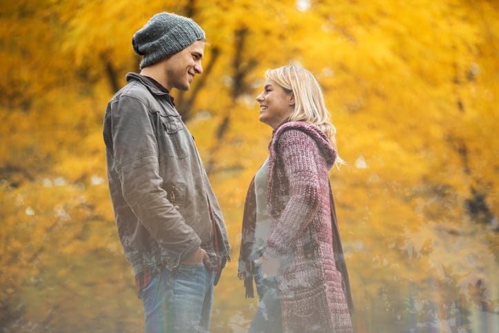 Young happy couple in autumn park talking to each other. The view is through the glass.