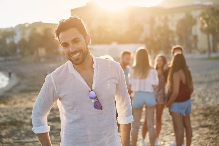 Portrait of handsome young man standing on beach with friends smiling