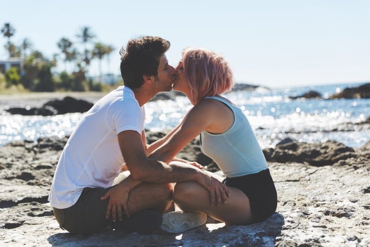 Profile portrait of couple sitting on beach kissing