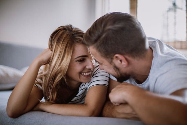 Happy Young Couple Flirting Under Bed Sheets In the Early Morning.