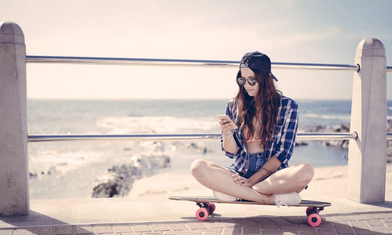 Skater girl checking her phone while sitting on her skateboard