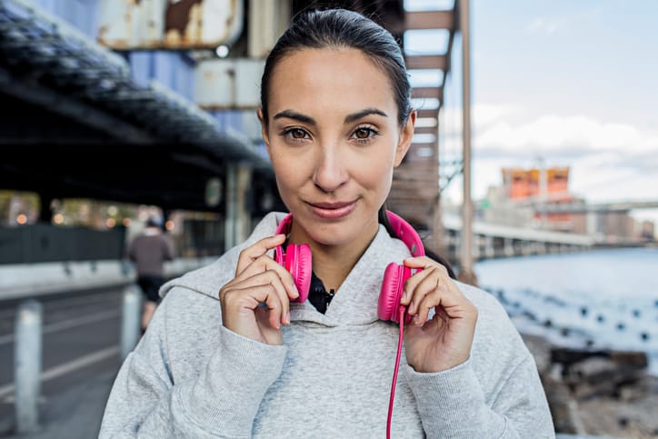 Close up portrait of confident young woman with headphone looking at camera. Fitness woman standing outdoors.