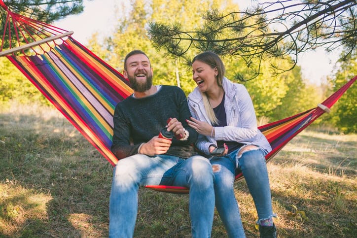 Young man and girl in orange hammock from back in beautiful forest