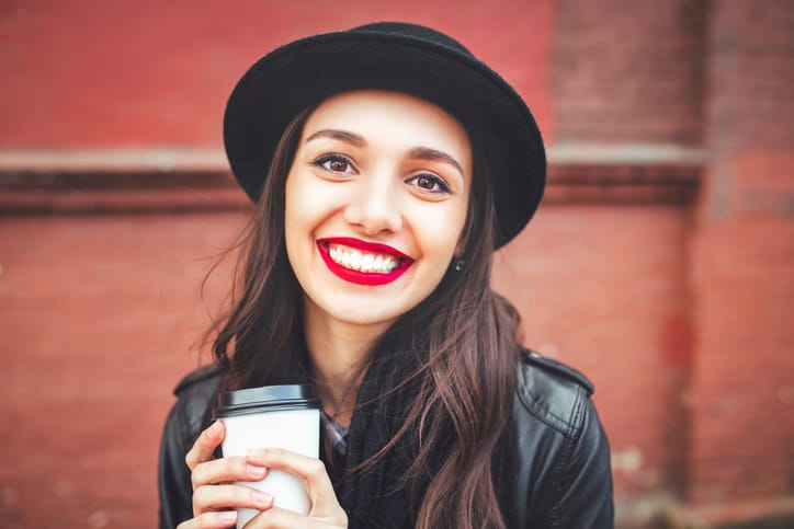 Trendy woman in hat with drink outdoor. Young woman with red lips in black hat