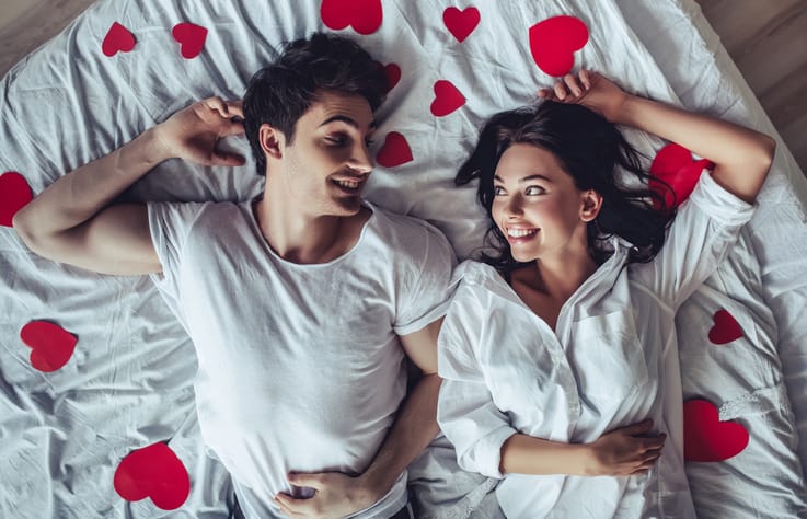 Man and woman laying on heart sheets.