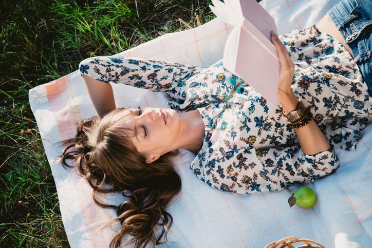 Woman laying outside reading a book.