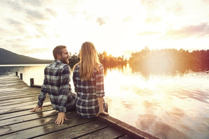 Young couple sitting on lake pier enjoying sunset