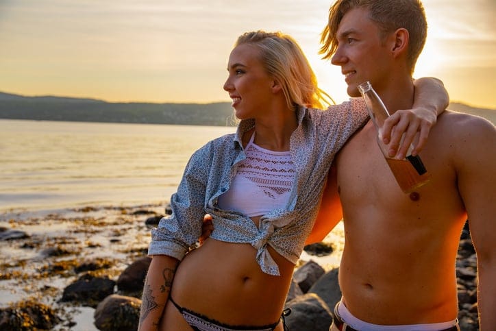Beautiful couple in embrace enjoys their vacation while drinking beer at the beach