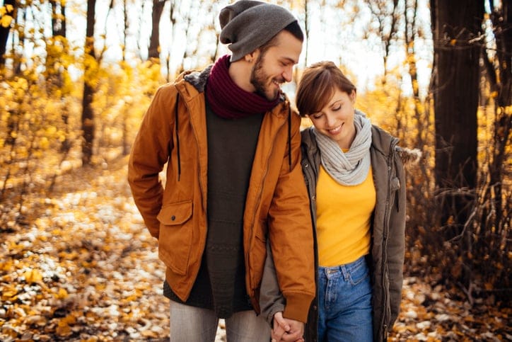 Couple happily walking through sunny forest in autumn