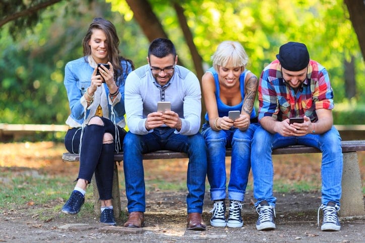Friends sitting in park and using smart phones