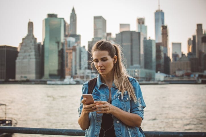 Woman in New York using smart phone in front of skyline at dusk