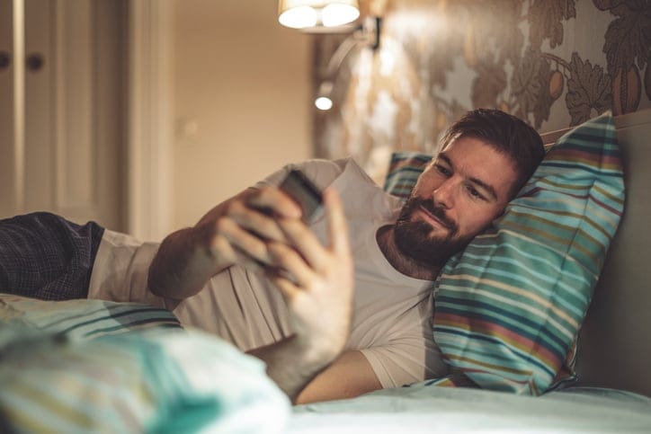 man with beard texting in bed