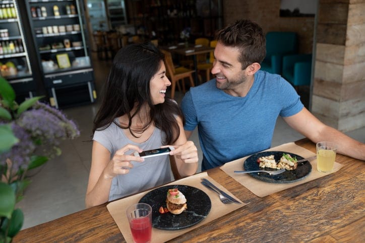 Happy couple at a restaurant taking a picture of their food
