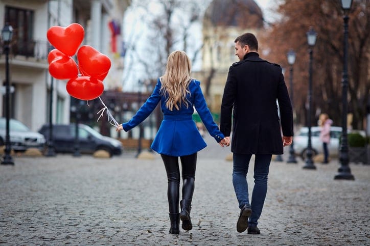 A young couple in a coat are holding a balloons heart in the cit