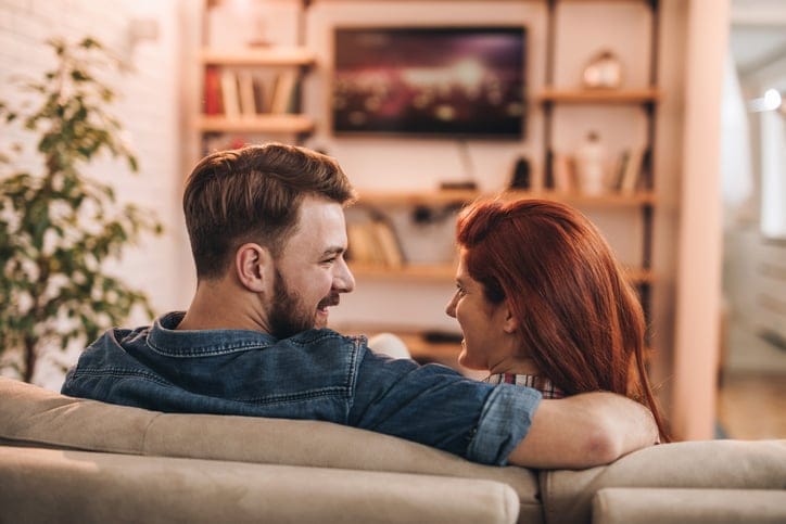 Couple talking while watching TV at home.