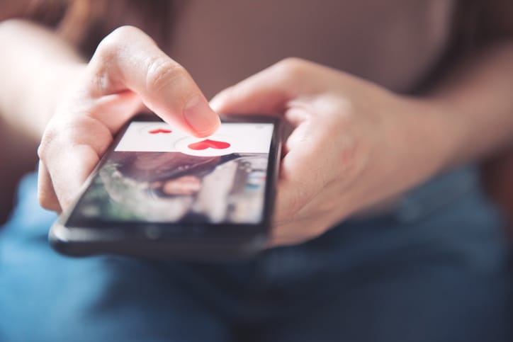 Finger of woman pushing heart icon on screen of smartphone.