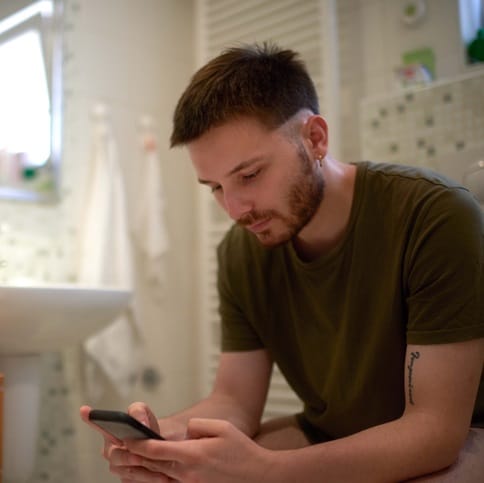 Man using his phone in the bathroom.