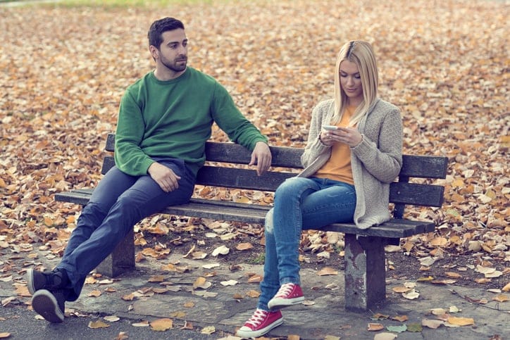man watching girl text on bench