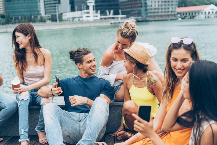 Multi-ethnic group of boys and girls hanging out, chatting, using smartphones and sharing great time together