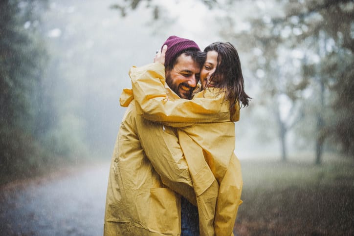 Couple embracing each other, smiling in the rain wearing raincoats