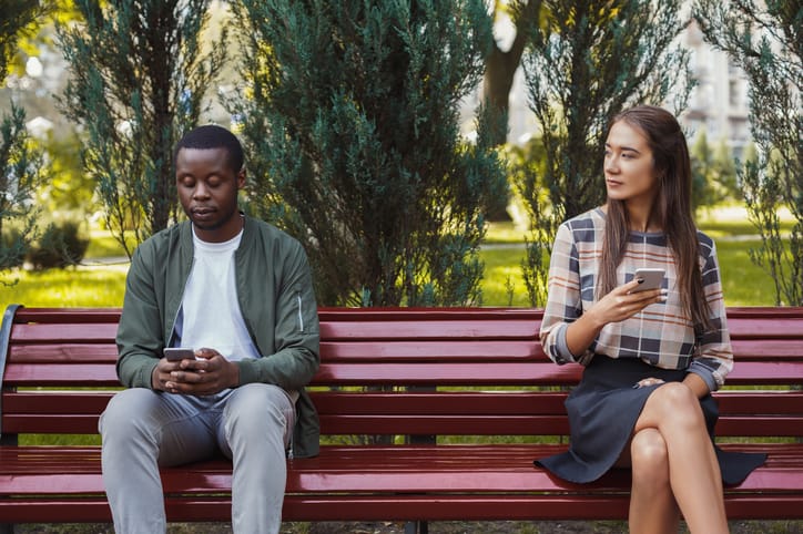 mixed race copule sitting on a bench texting