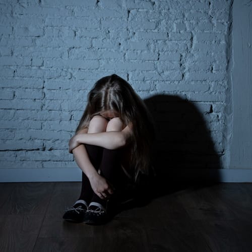Sad desperate young girl suffering from bulling and harassment felling lonely, unhappy desperate and hopeless sitting against the wall, dark light. School isolation, abuse and bullying concept (Sad desperate young girl suffering from bulling and haras