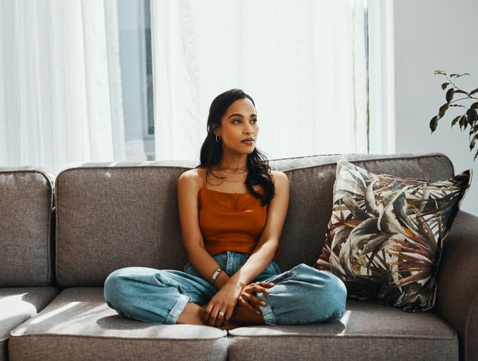 Shot of a young woman looking thoughtful while relaxing on the sofa at home